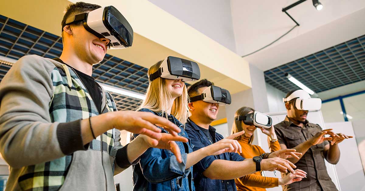 Five people wearing virtual reality headsets stand in a row, smiling and holding their hands out as if interacting with objects in a lifelike simulation.