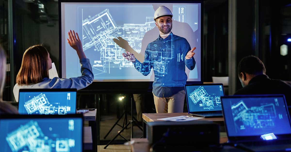 A man in a hard hat presents architectural blueprints on a screen to a workforce using laptops in a modern office setting.