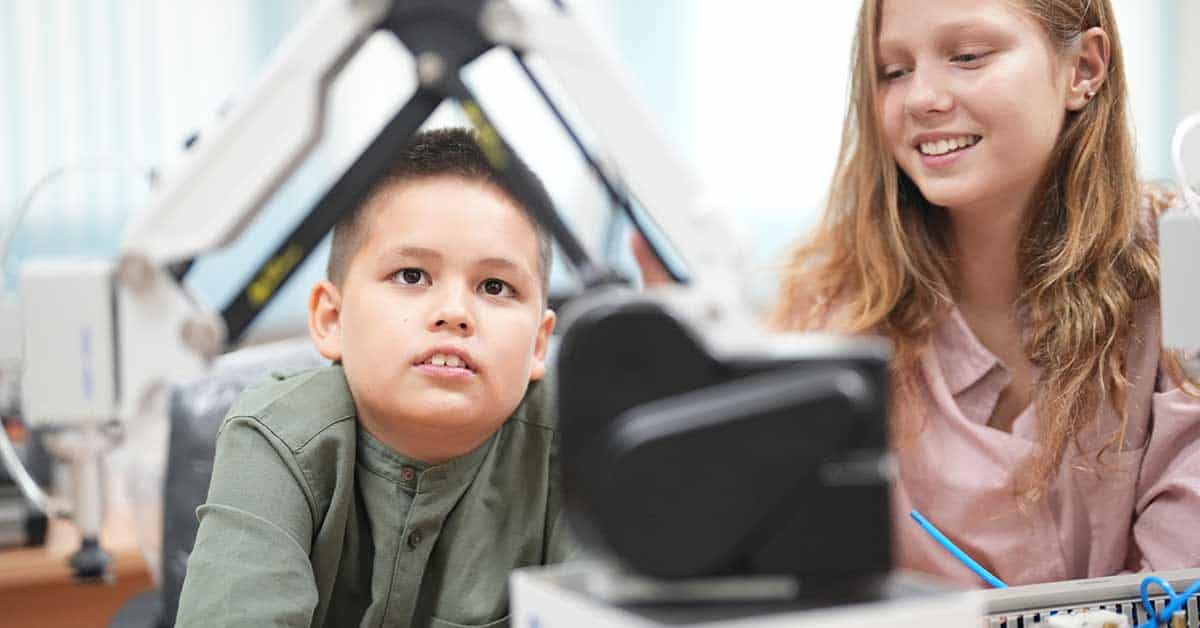 Two children engage in a robotics activity, focused on a mechanical device in the classroom, where they explore the principles of Ethical AI.