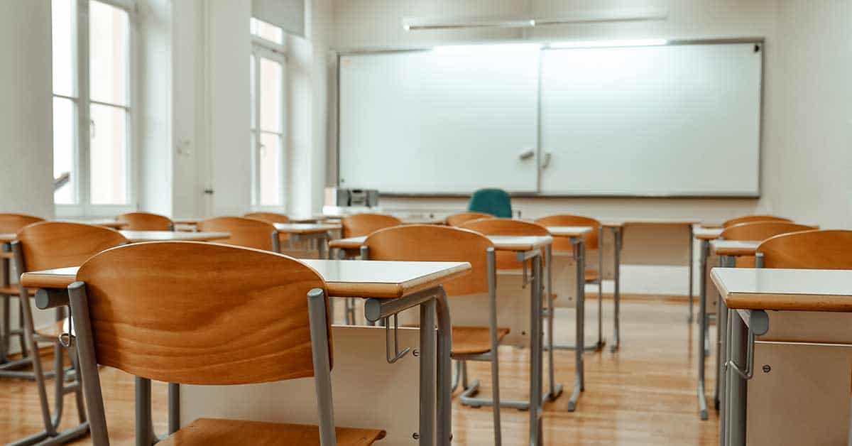 Empty classroom with wooden desks and chairs, a whiteboard at the front, and natural light coming through large windows creates an inviting setting for education.