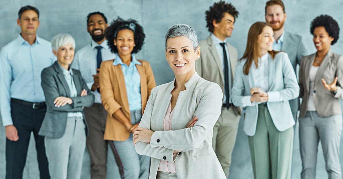 A group of professionally dressed people stands together, showcasing leadership, with a woman in a light suit confidently smiling at the front.