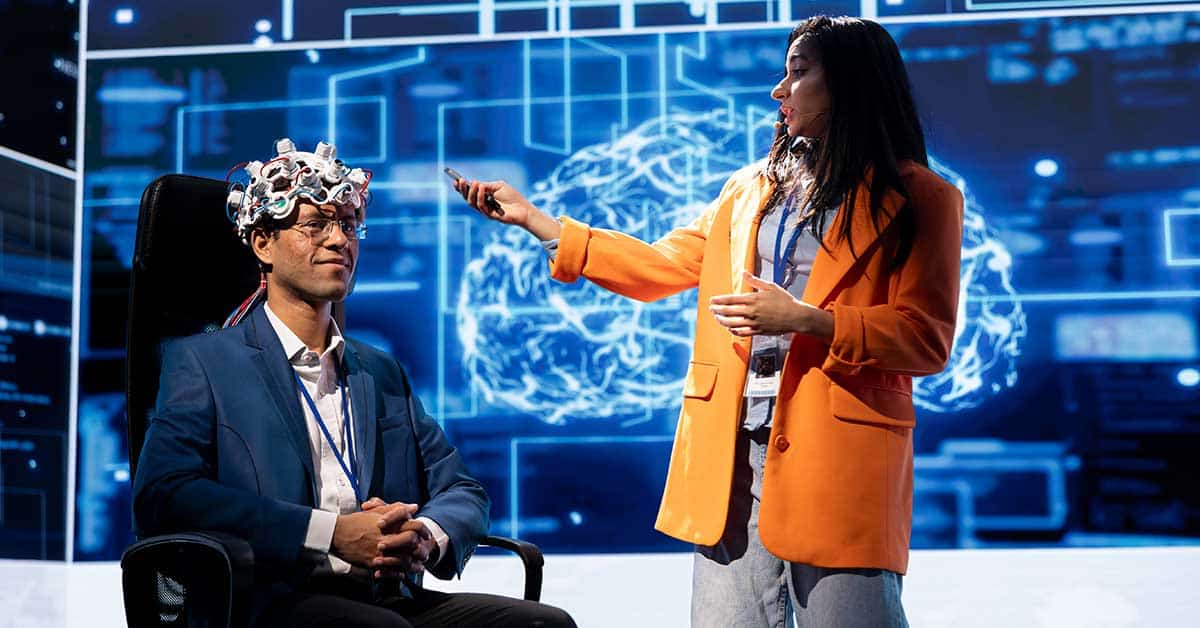 In an AI-driven future, a person wearing a brain-monitoring device sits in a chair while another stands beside them, gesturing in front of an educational digital brain display.