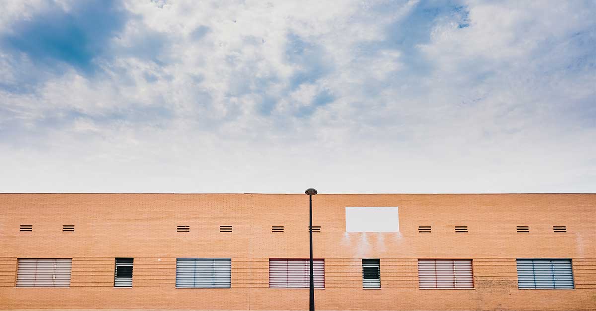 A brick building with several barred windows and a white rectangular patch near the roof stands under a partly cloudy sky, exuding an air of bureaucracy.