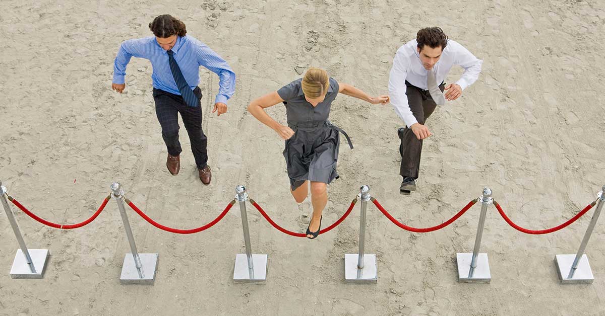 Hiring hurdles for three individuals in business attire leap over a red rope barrier on a sandy surface, viewed from above, as if navigating the complex landscape of tribal adjudication with agility and finesse.