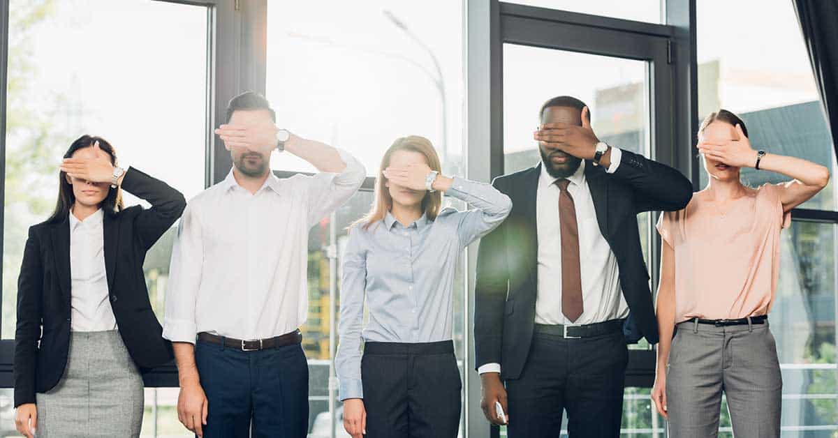 Five people standing indoors, each covering their eyes with one hand, dressed in business attire—contemplating the tricky terrain of retaliatory job references.