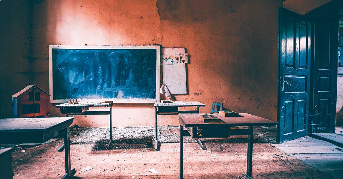 An abandoned classroom with dusty desks, a worn chalkboard, and an open door letting in light, once vibrant with the future workforce preparing for their dreams.