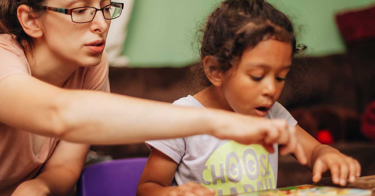 An adult wearing glasses is helping a young child with a puzzle. The child, focused on the puzzle, is wearing a T-shirt that reads "Choose Happy." Their shared laughter feels like a superpower, bridging gaps and fostering connections beyond words.