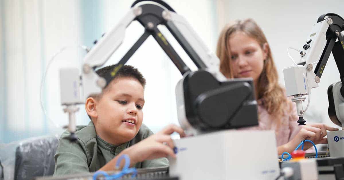 In a classroom setting, two children engage with robotic arms, offering a glimpse into the future of education where young minds are nurtured to join a tech-savvy workforce.