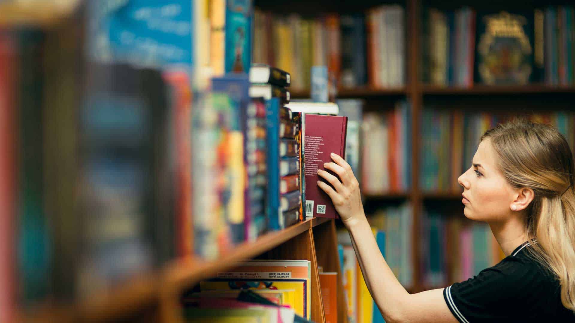 A person is selecting a book from a library shelf, surrounded by rows of colorful books.